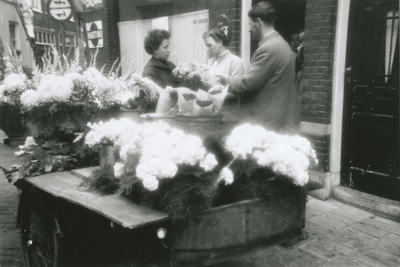 875287 Portret van mevr. Veenendaal-van Zuilen (Rozenstraat 21) met twee klanten bij haar bloemenkar op de hoek van de ...